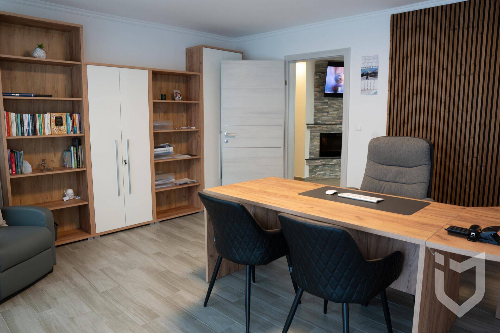 Helles Büro mit Holzregalen, modernem Schreibtisch und Blick in einen weiteren Raum.