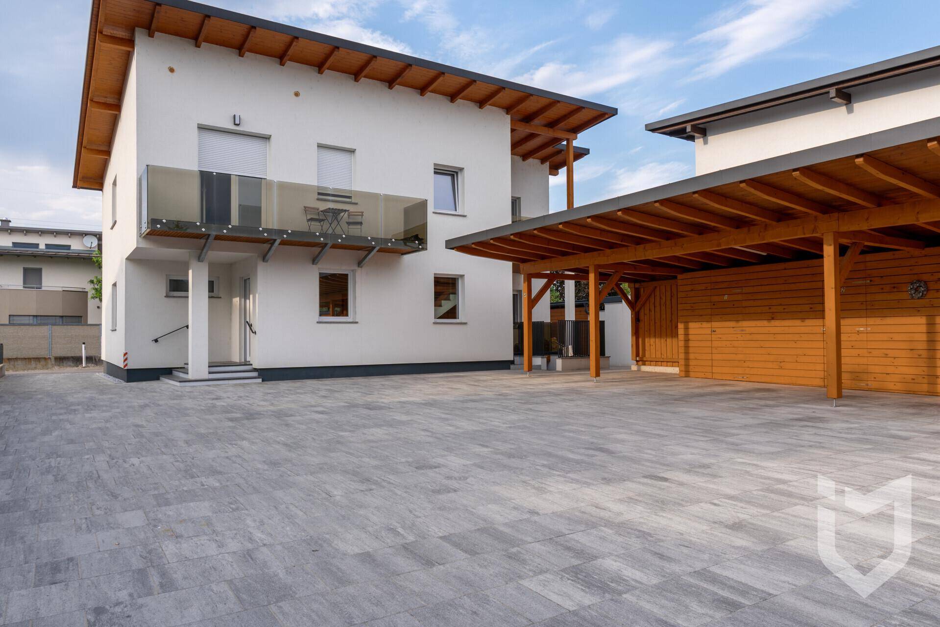 Moderne Hausfassade mit großem Carport aus Holz und gepflasterter Zufahrt.