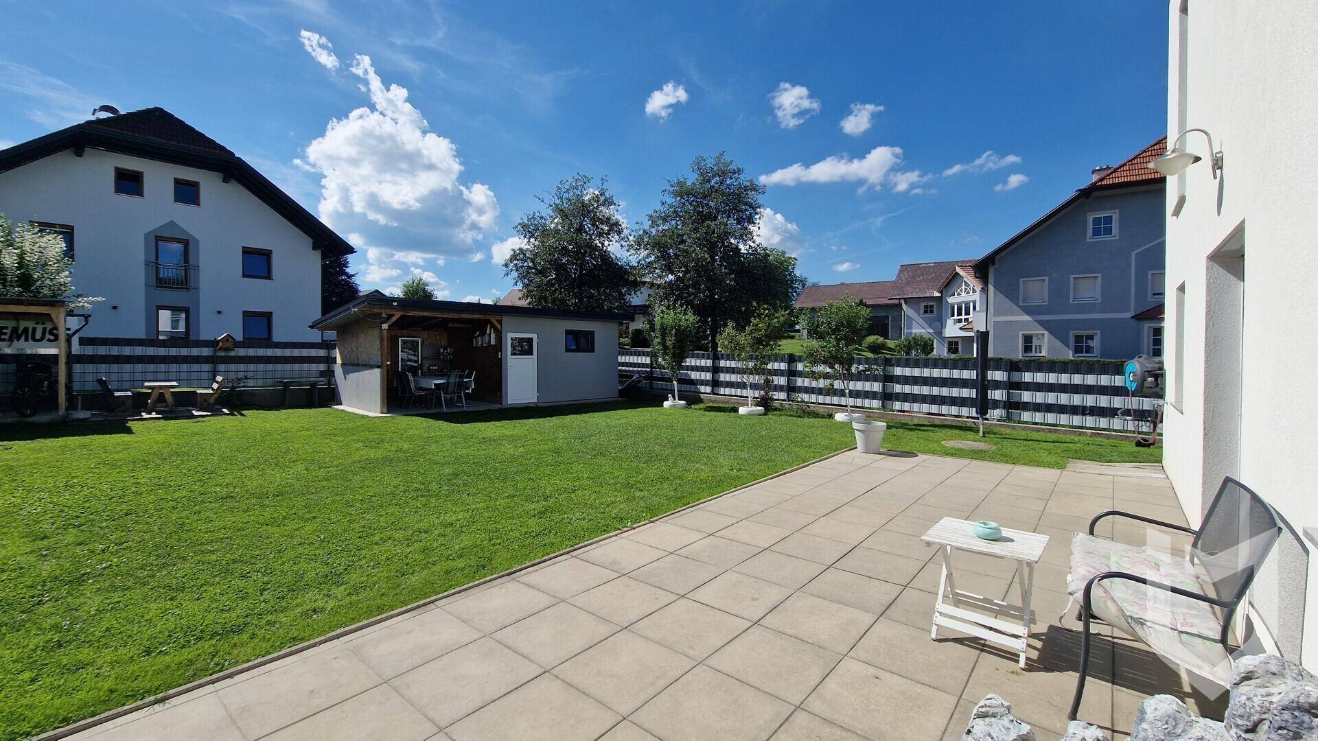 Gepflegter Garten mit großer Rasenfläche, Terrasse und einem gemütlichen Gartenhaus.