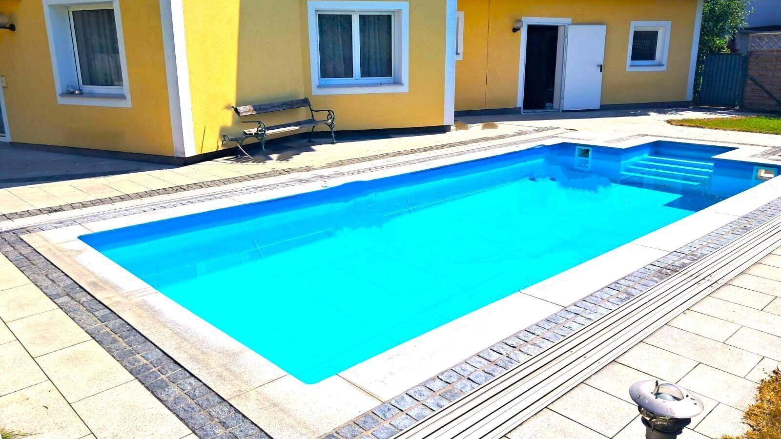 Großzügiger Poolbereich mit gefliester Umrandung und klarem, blauem Wasser.