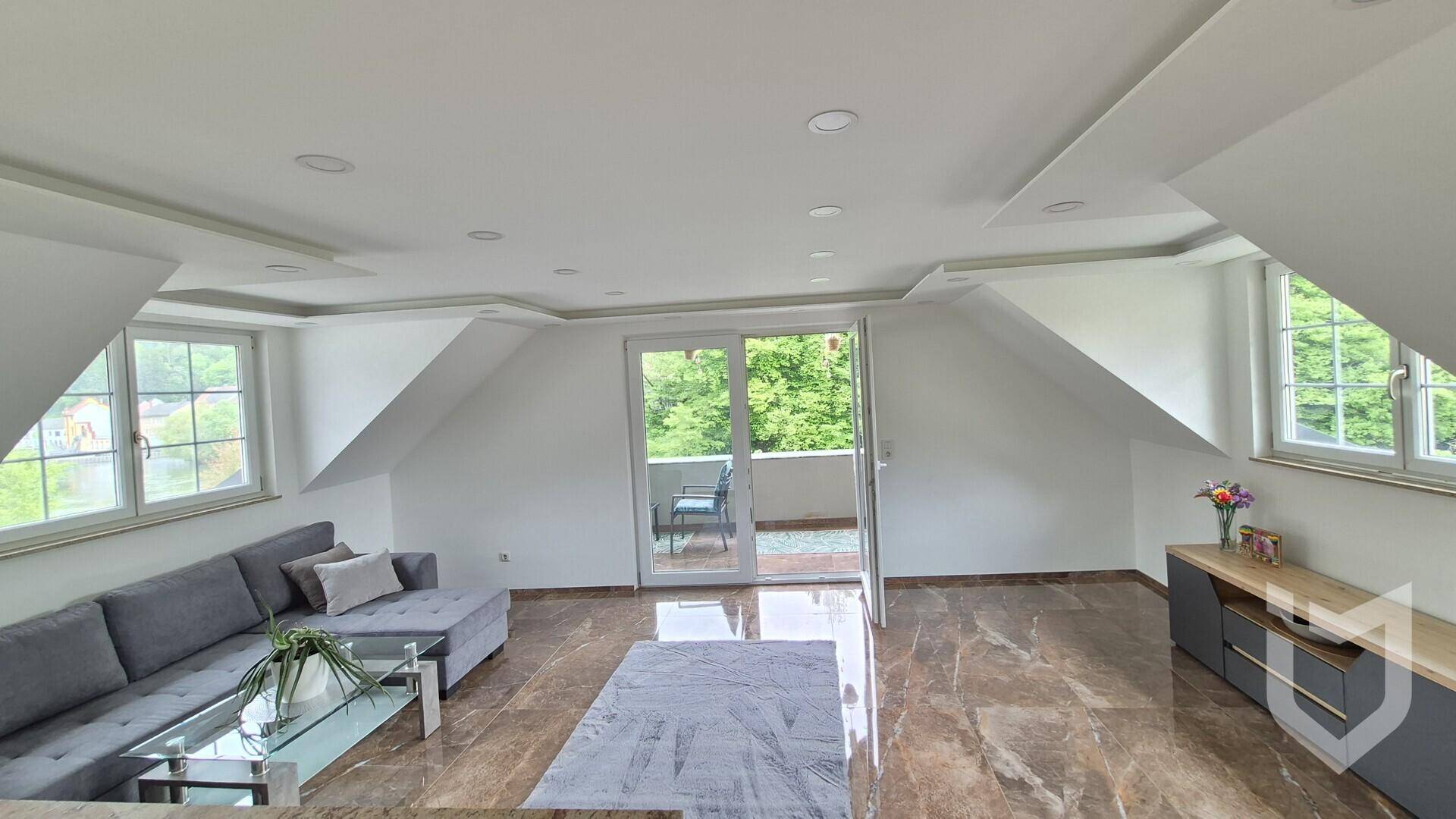 Helles Wohnzimmer im Dachgeschoss mit Zugang zu einem kleinen Balkon und Blick ins Grüne.