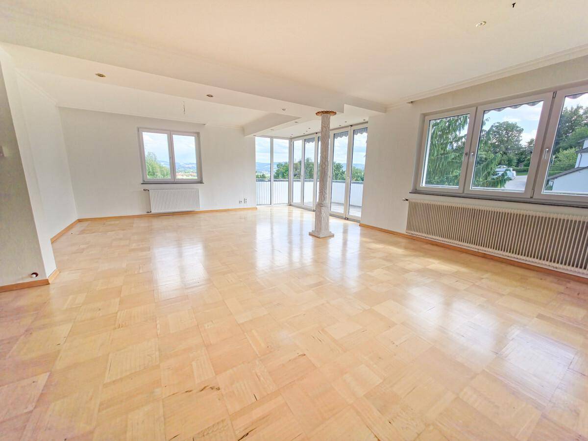 Weitläufiges Wohnzimmer mit Parkettboden, großen Fenstern und Zugang zum Balkon mit Aussicht.