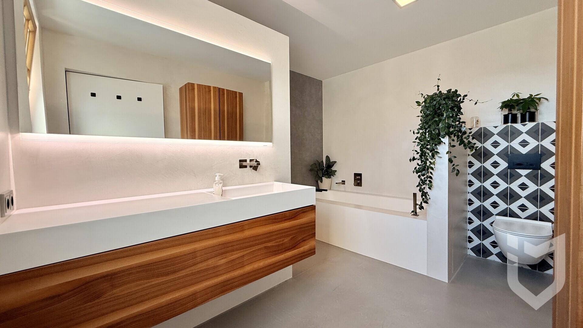 Elegantes Badezimmer mit breitem Waschtisch, großem Spiegel und integrierter Badewanne.