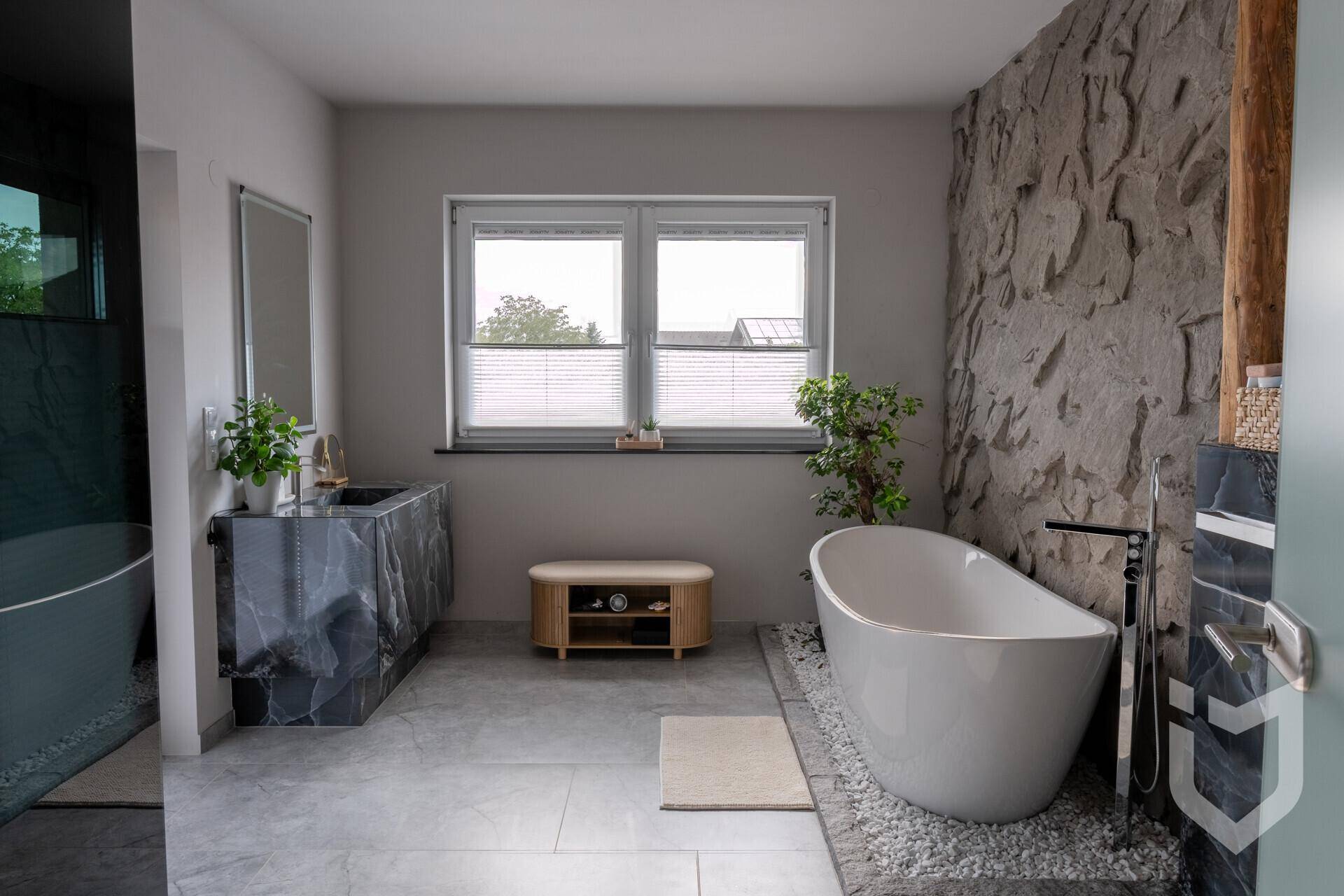 Luxuriöses Badezimmer mit freistehender Badewanne, Steinwand und modernem Waschtisch.