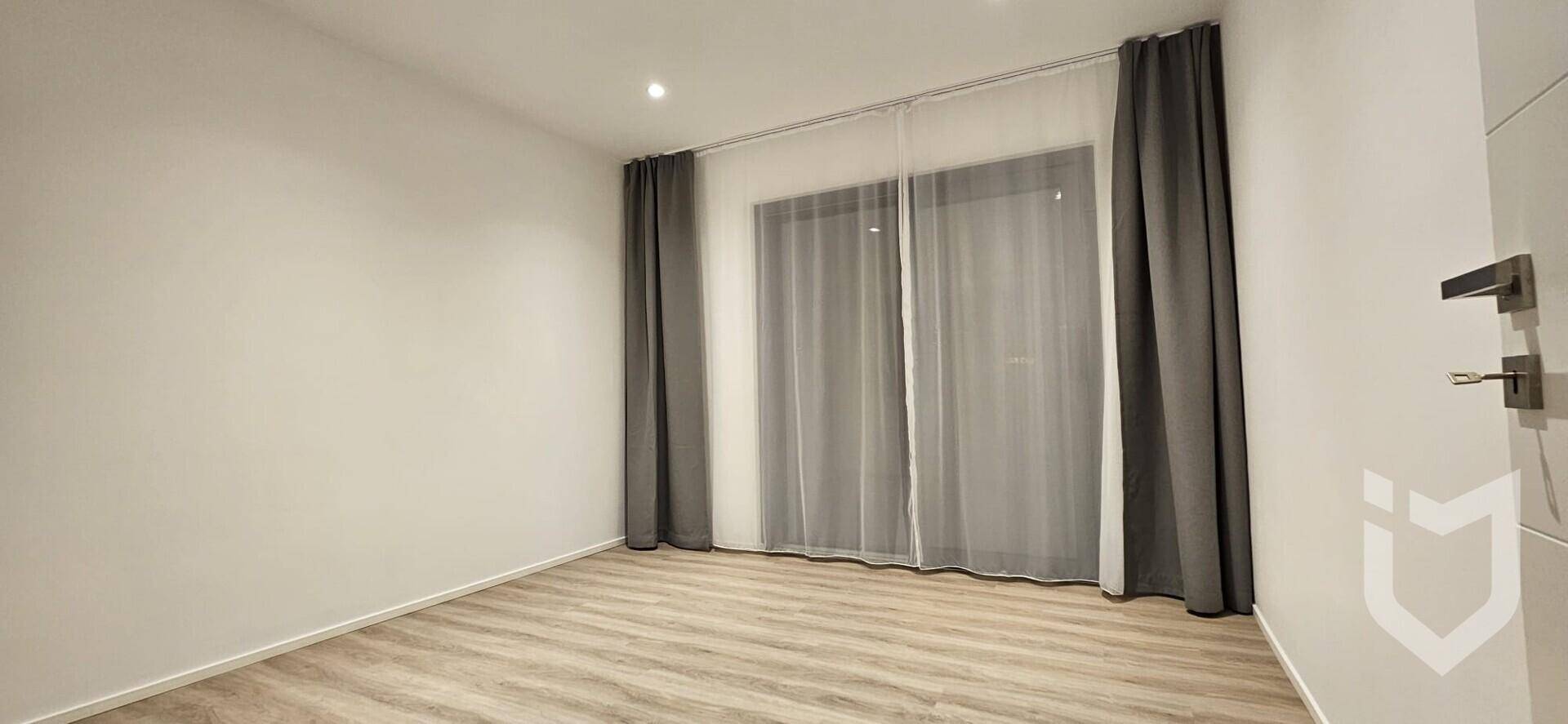 Geräumiges Zimmer mit hellem Laminatboden und großen Fenstern für viel Tageslicht.