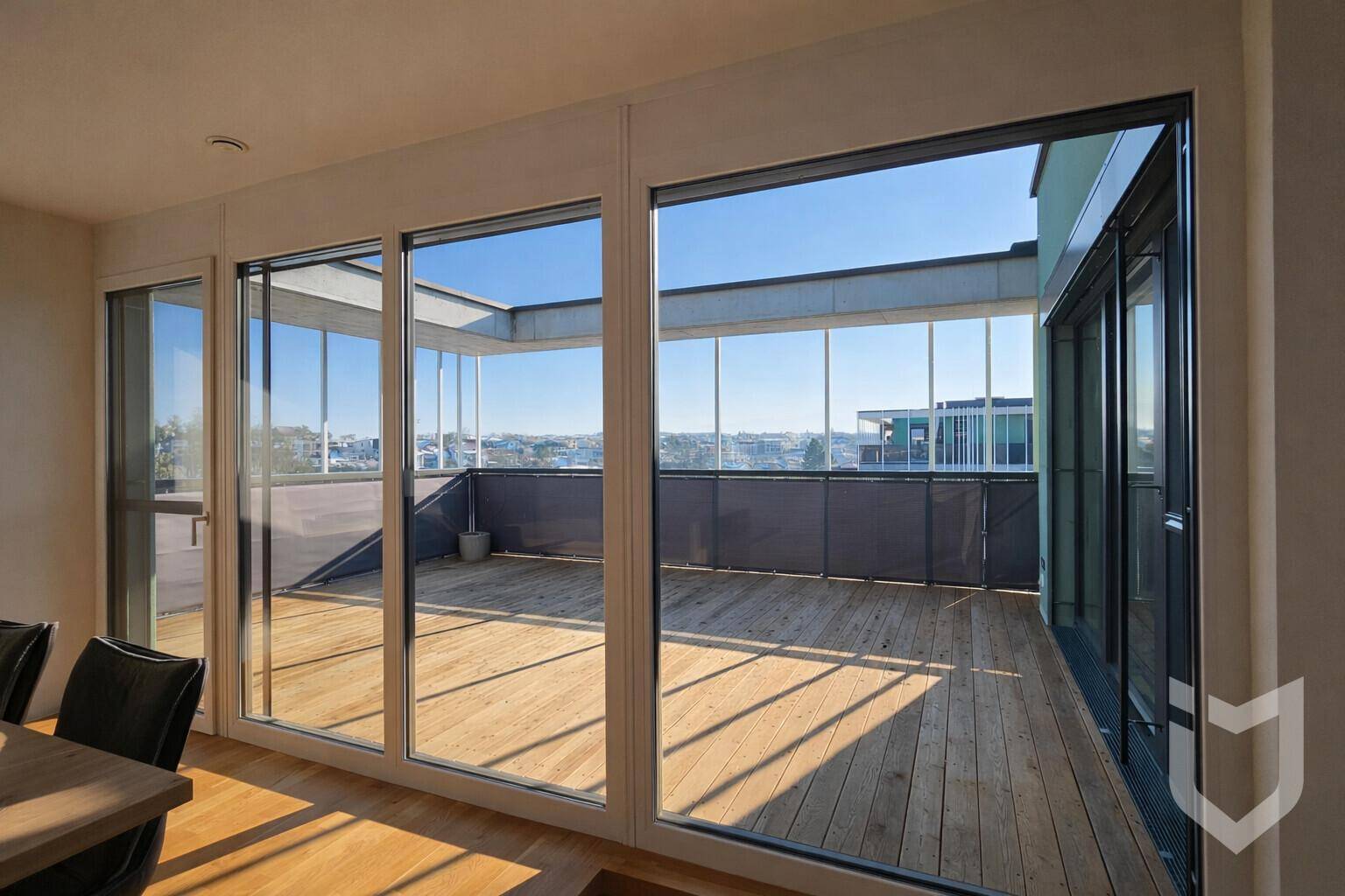Heller Innenraum mit großen Glasfronten, die den Blick auf eine weitläufige Holzterrasse freigeben.