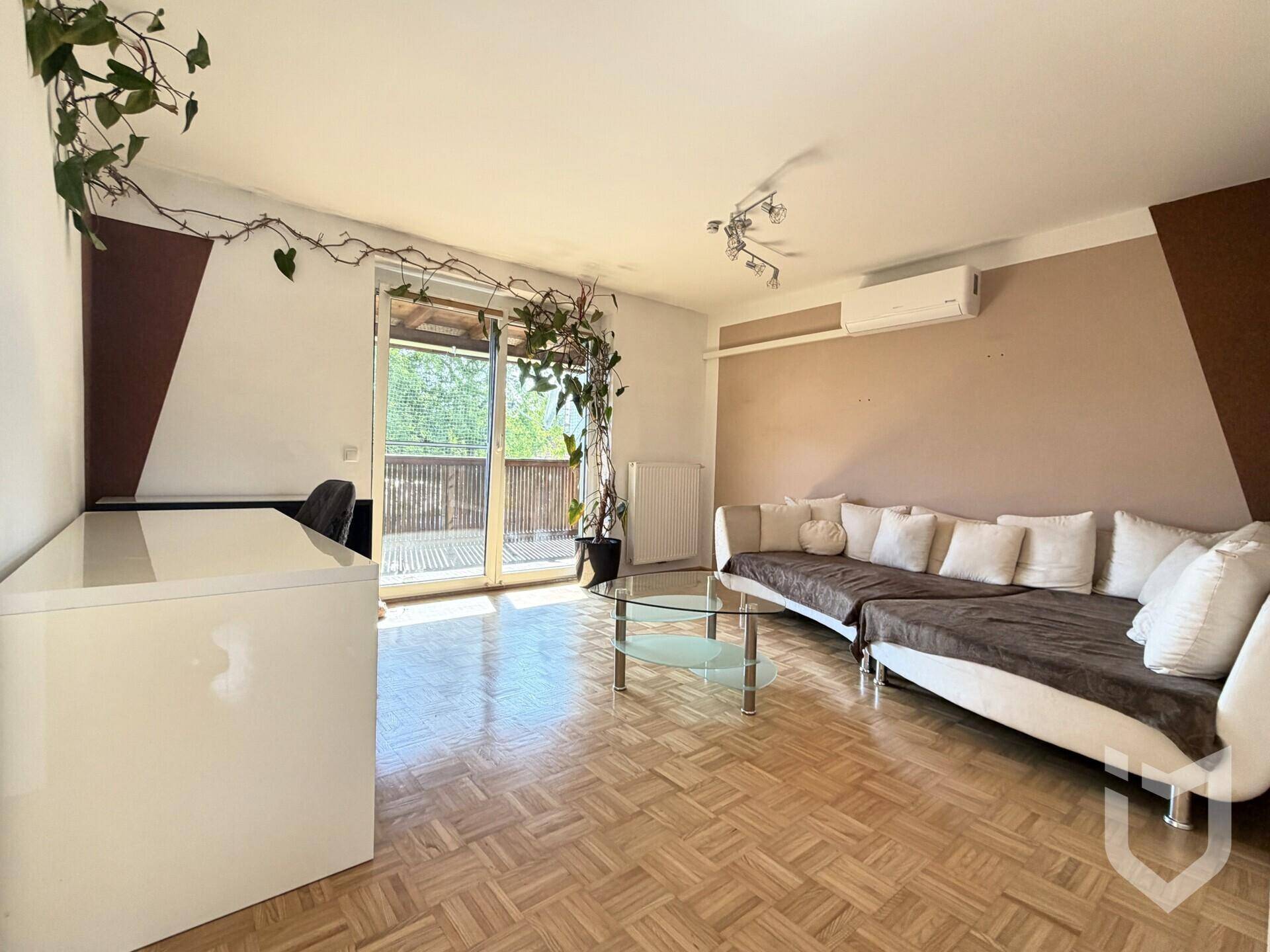 Helles Wohnzimmer mit Parkettboden, bequemer Couch, Klimaanlage und Zugang zum Balkon.
