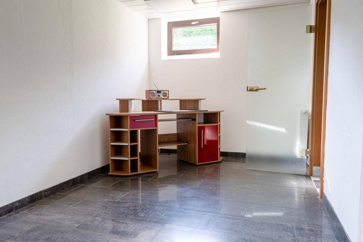Kleines Büro oder Arbeitszimmer mit Schreibtisch und Fliesenboden, gut beleuchtet.