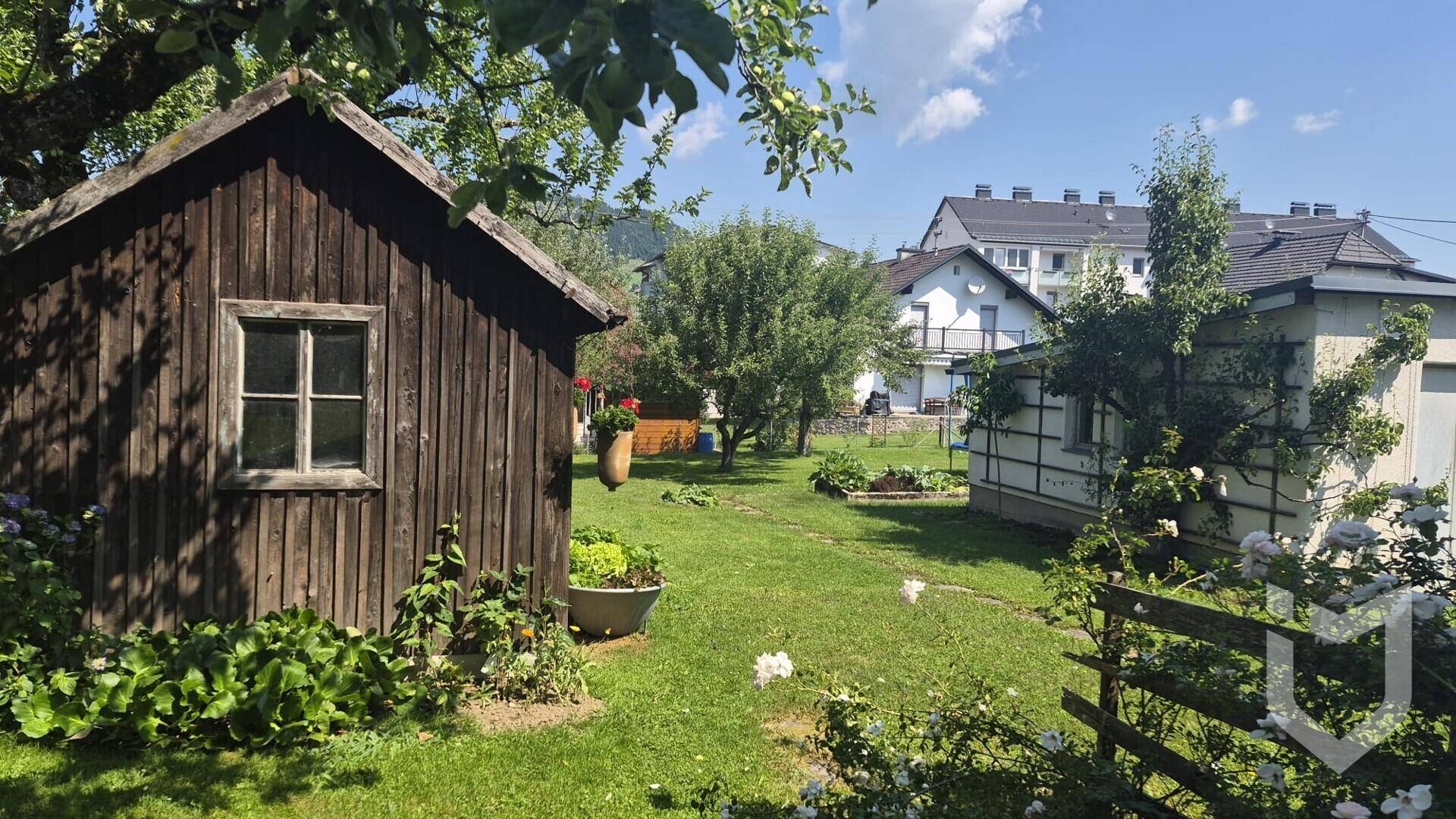 Idyllischer Gartenbereich mit Holzschuppen, grüner Rasenfläche und blühenden Rosen.