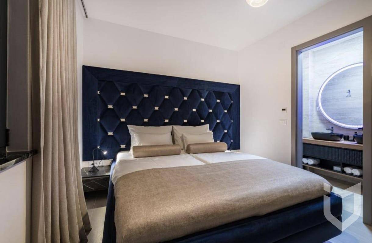 Schlafzimmer mit großem blauem Kopfteil und direktem Zugang zu einem modernen Badezimmer.