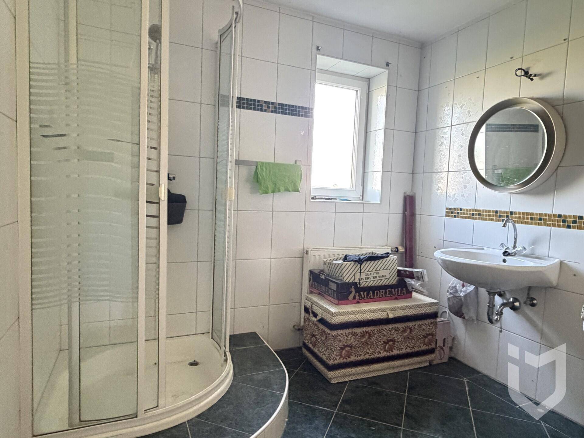 Badezimmer mit weiß gefliesten Wänden, Duschkabine und Fenster für Tageslicht.