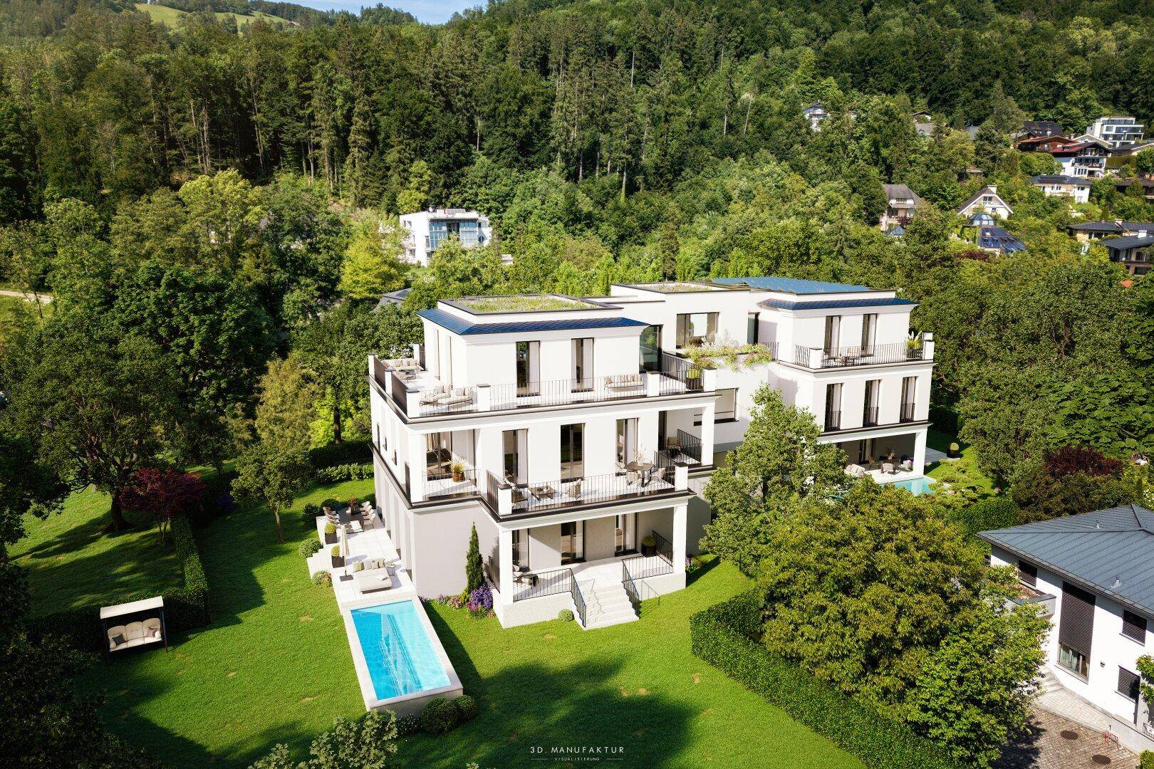 Luftaufnahme einer modernen Wohnanlage mit Pool und weitläufigen Grünflächen vor bewaldeten Hügeln.