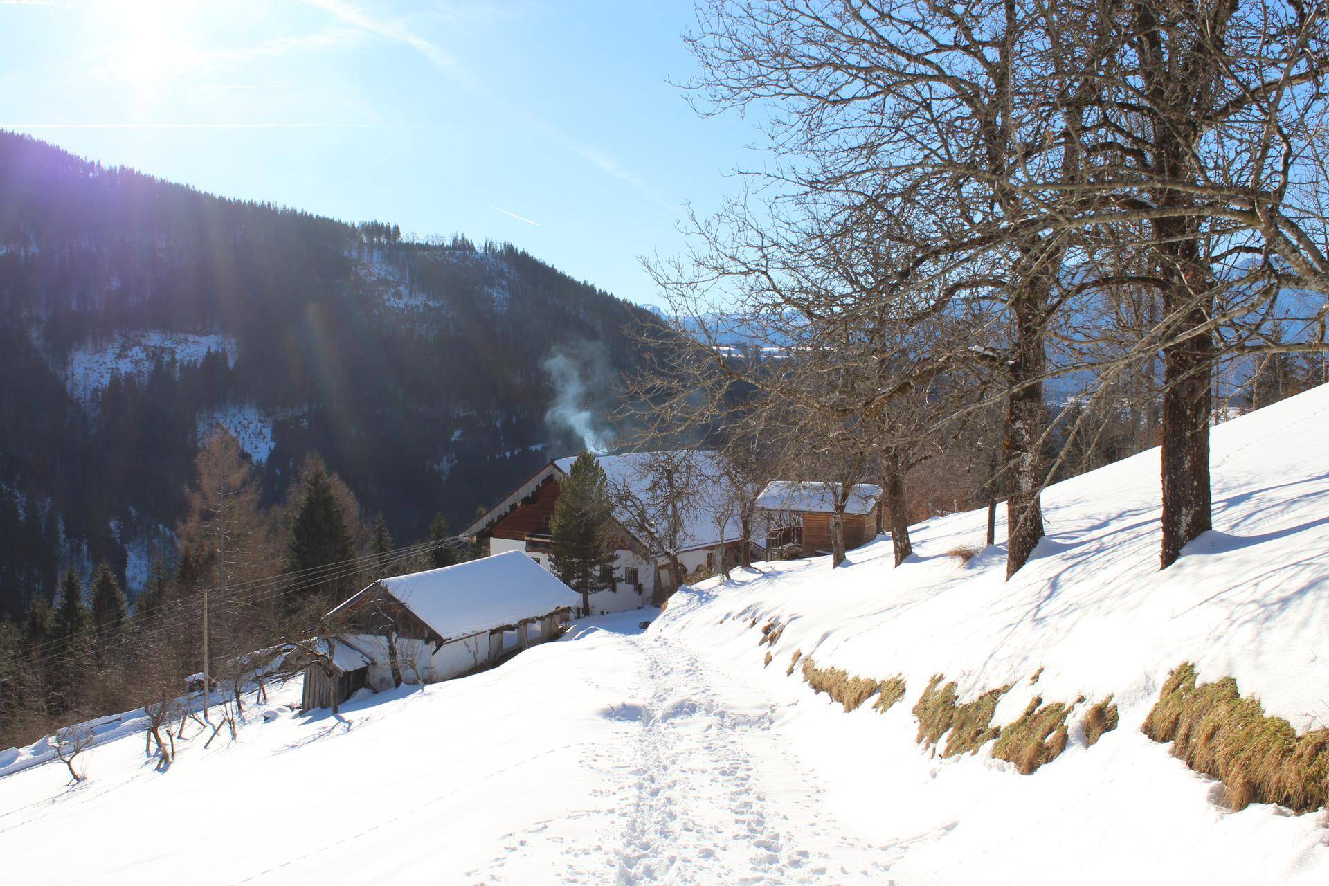 Verschneite Landschaft mit traditionellen Häusern und Bergen im Hintergrund an einem sonnigen Wintertag.