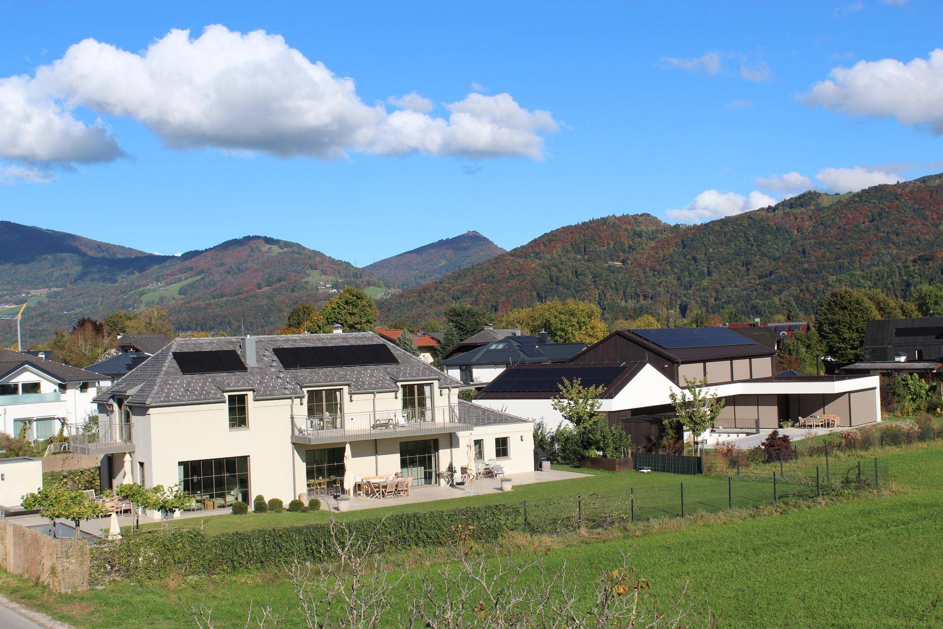 Wohngebiet mit modernen Häusern, grünen Gärten und einer malerischen Bergkulisse.