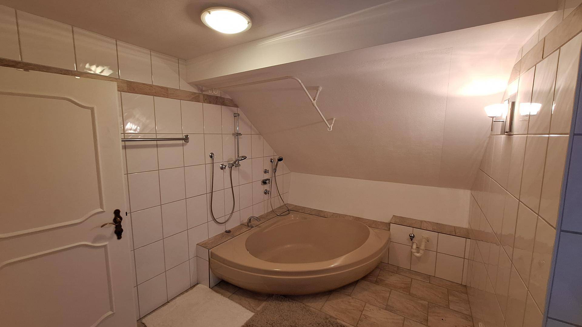 Badezimmer im Dachgeschoss mit Eckbadewanne, weißen Fliesen und schrägen Wänden.
