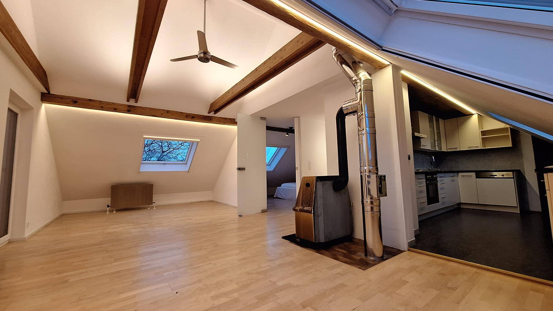 Geräumiger Wohnbereich im Dachgeschoss mit Kaminofen und offenem Übergang zur Küche.