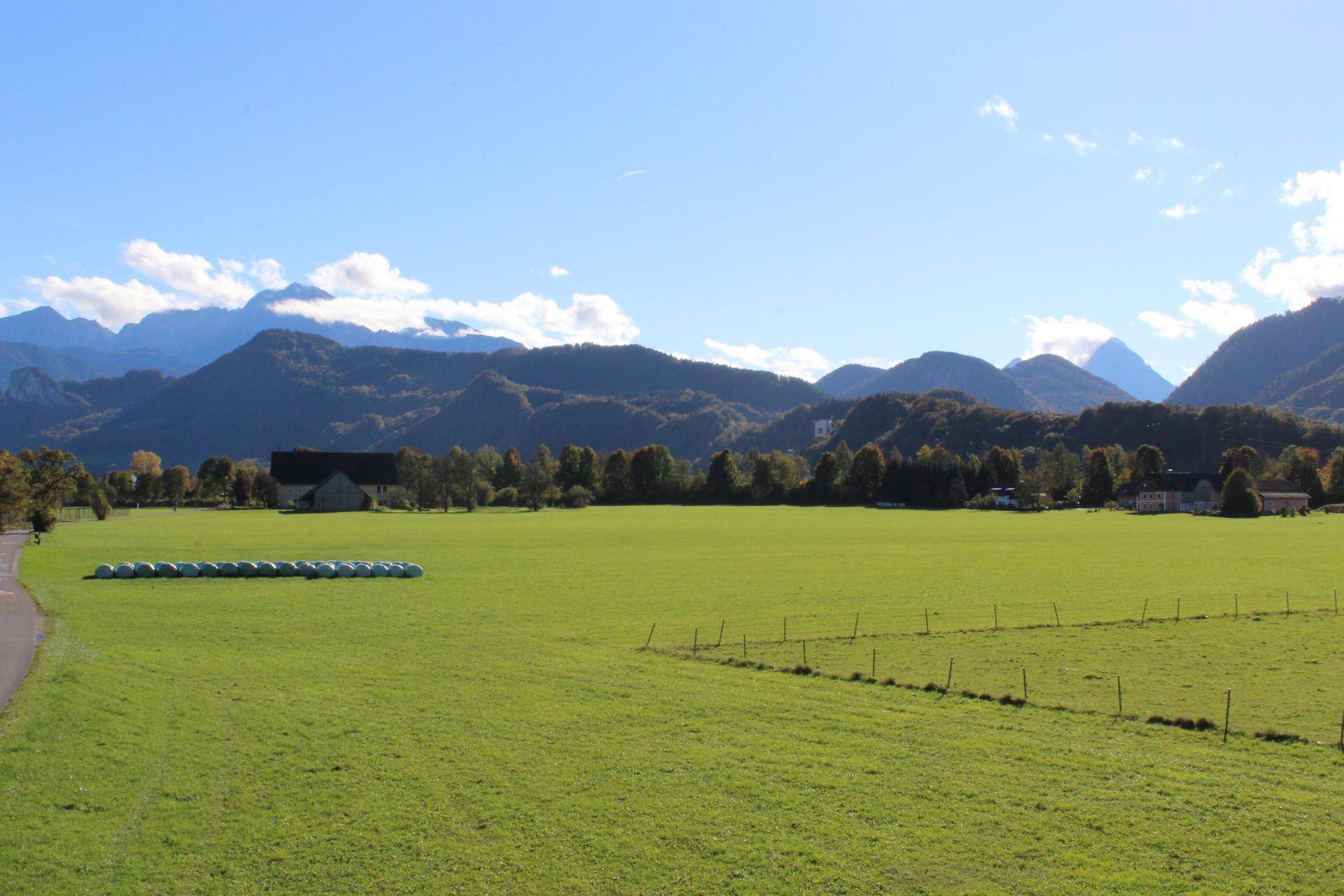 Weitläufige Landschaft mit grünen Feldern und majestätischen Bergen unter blauem Himmel.