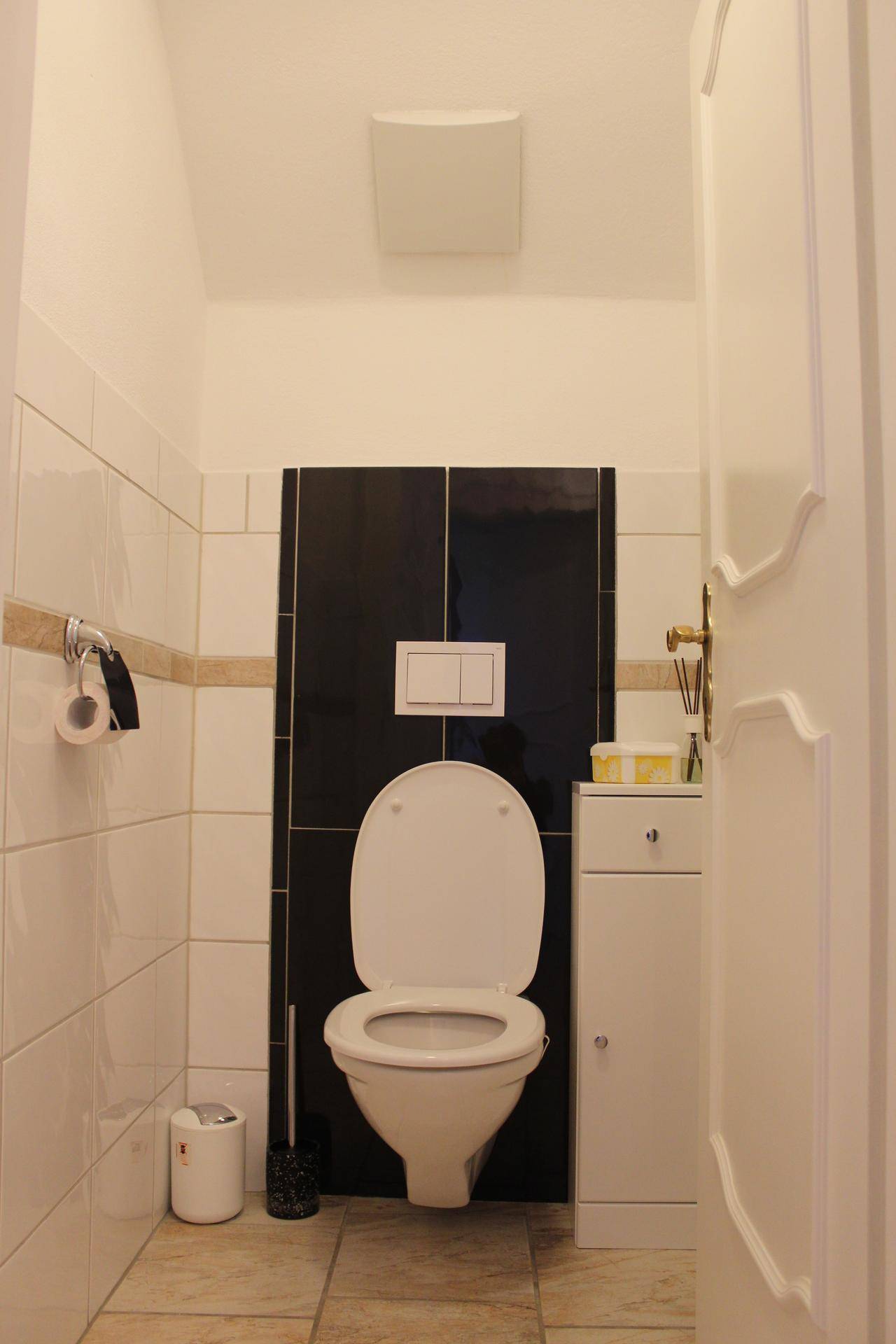 Separate Gästetoilette mit wandmontiertem WC und schwarz-weißen Fliesen.