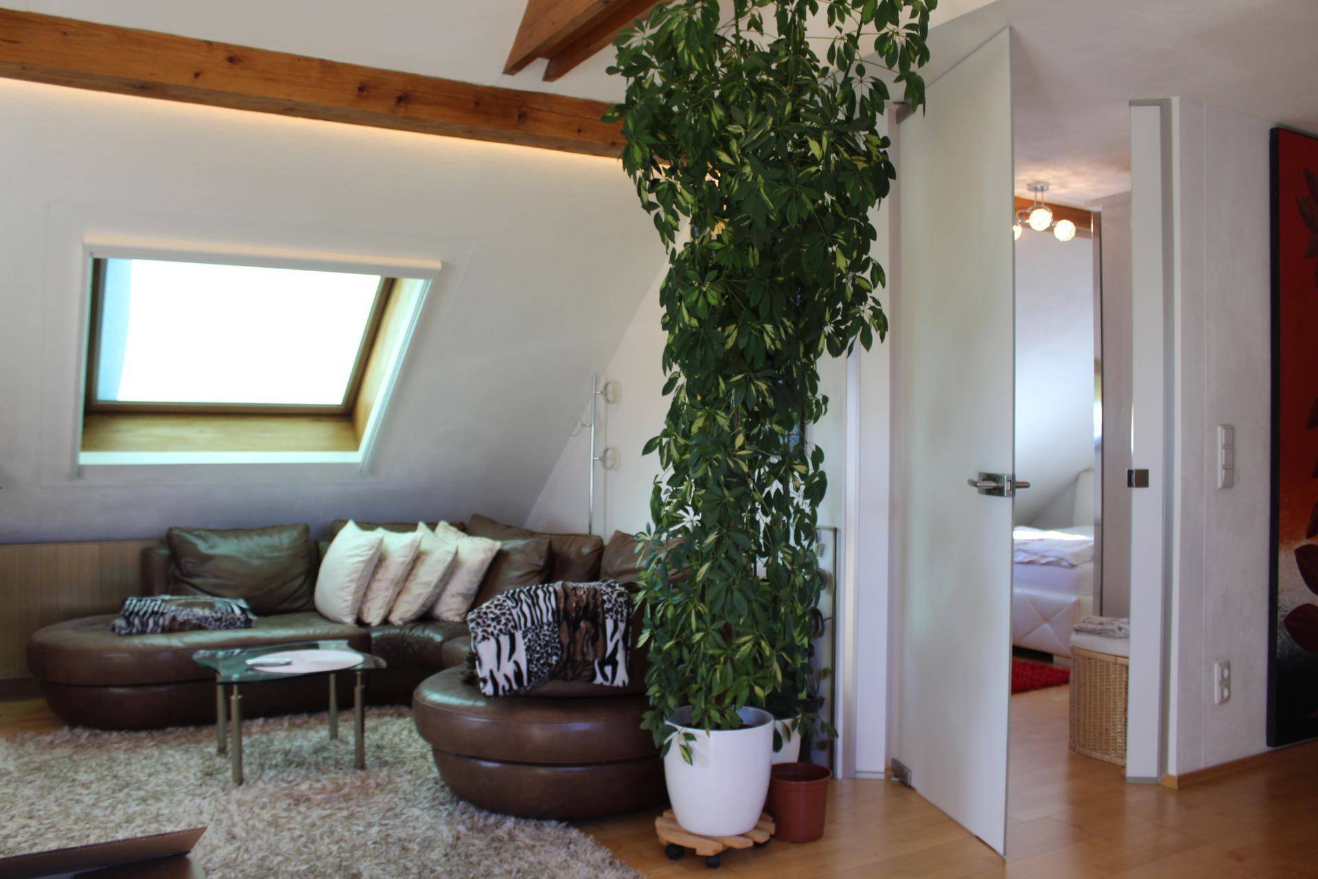 Gemütliches Wohnzimmer im Dachgeschoss mit Ledersofa, Holzbalken und großem Fenster.