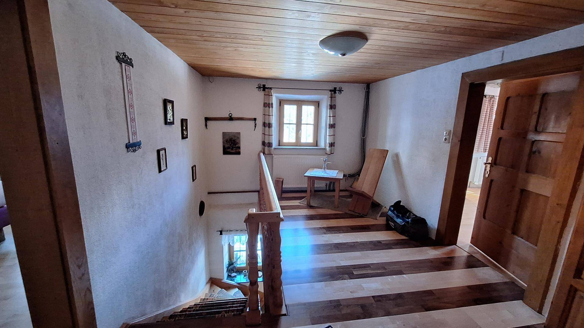Oberer Flur mit Holztreppe, Holzboden und einem Fenster, das Tageslicht hereinlässt.
