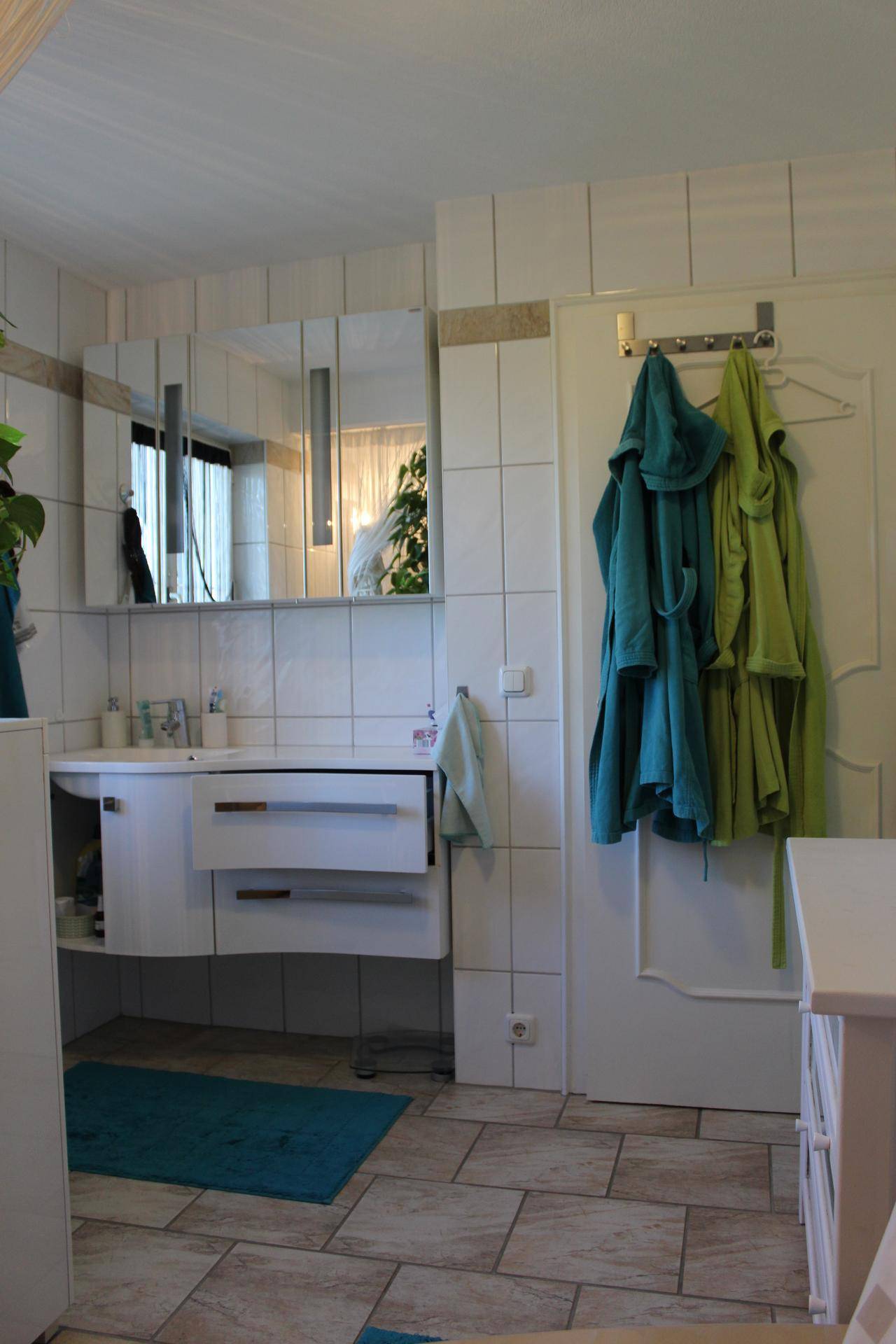 Modernes Badezimmer mit weißem Waschtisch, Spiegelschrank und hellen Fliesen.