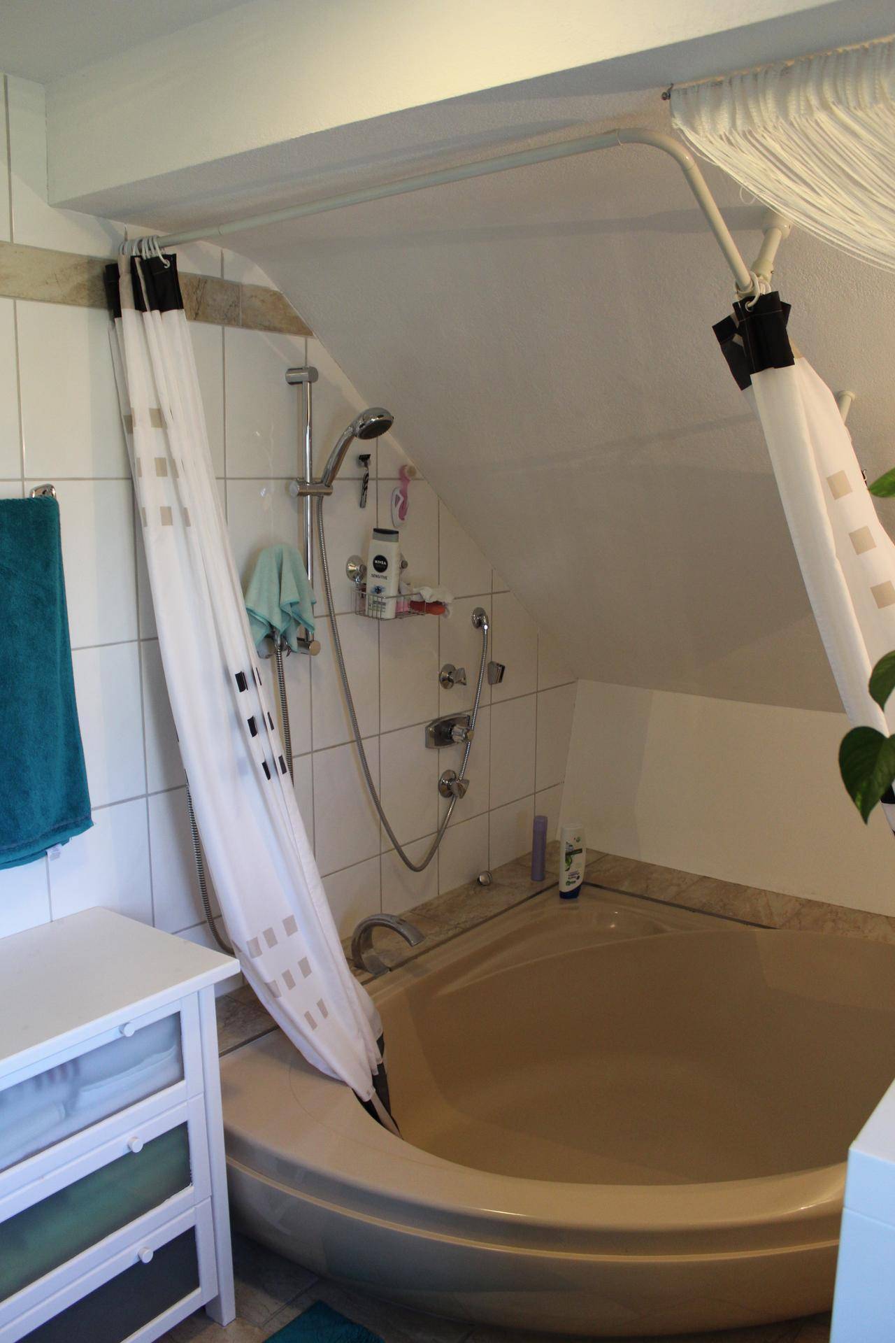 Badezimmer im Dachgeschoss mit Eckbadewanne, Duschvorhang und schrägen Wänden.