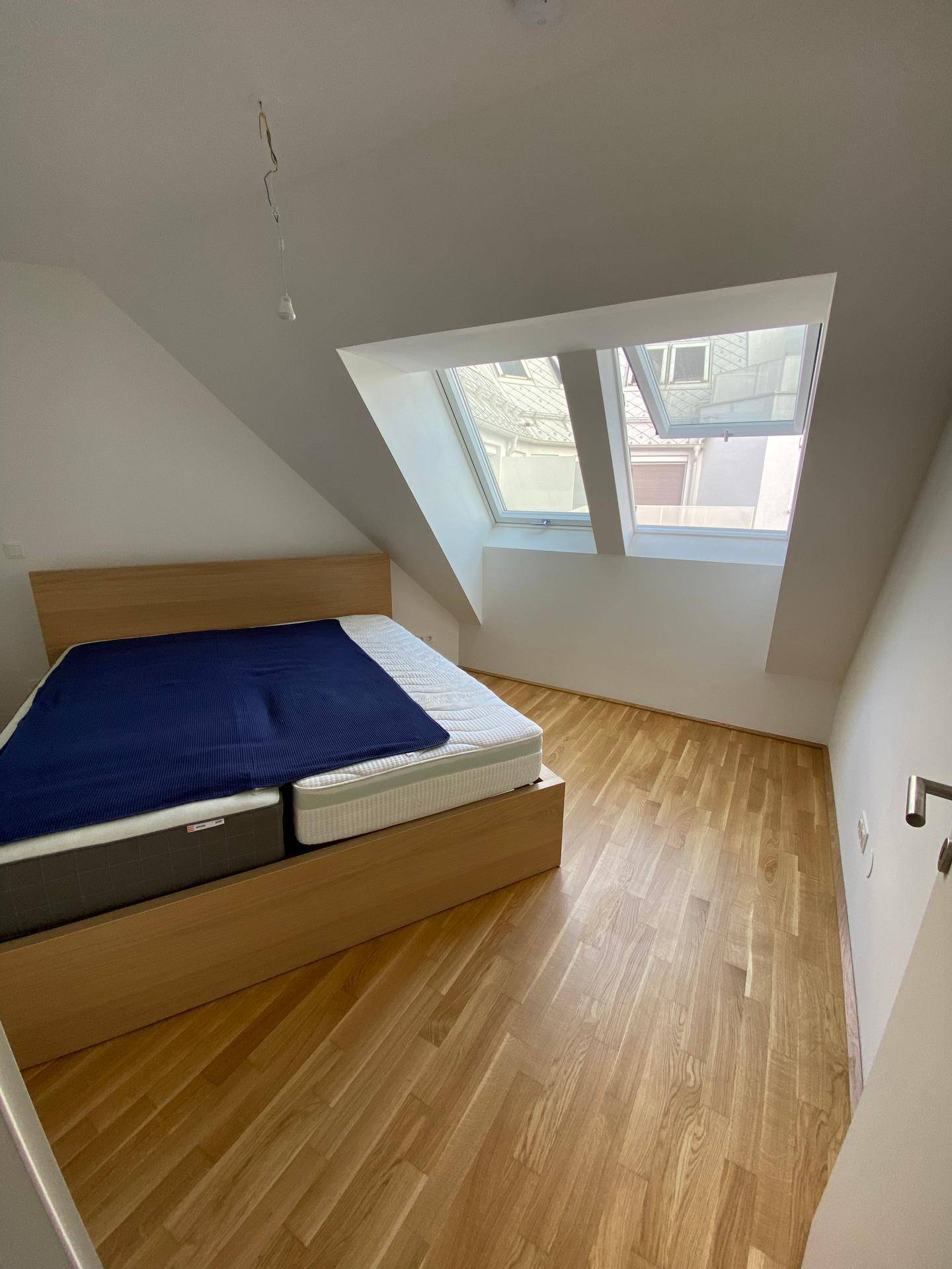 Schlafzimmer mit Holzbett, Holzboden und zwei Dachfenstern, die viel Licht hereinlassen.