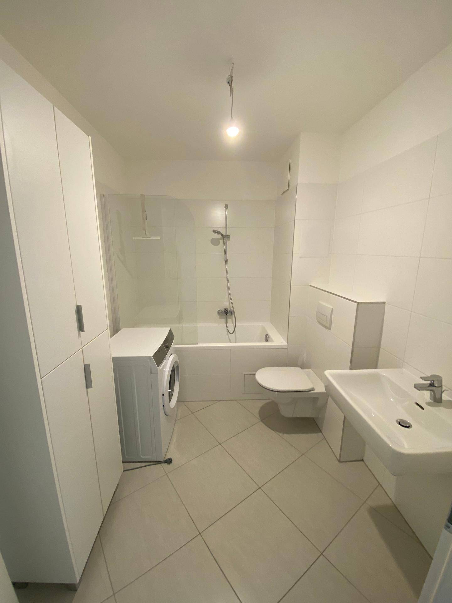Helles Badezimmer mit Badewanne, WC, Waschbecken und Waschmaschine, komplett gefliest.
