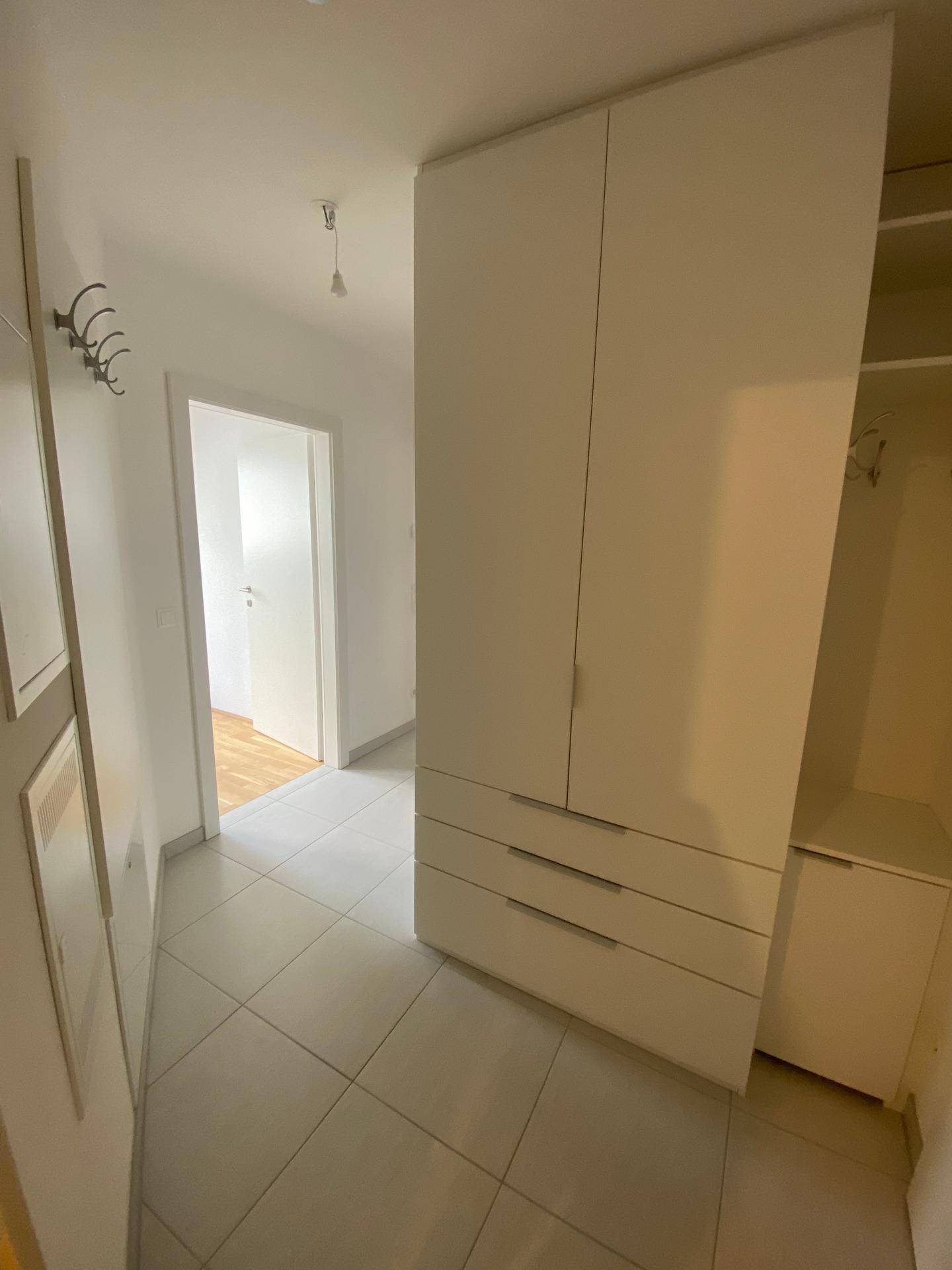 Heller Flur mit Einbauschrank und hellen Fliesen, der zu weiteren Räumen führt.