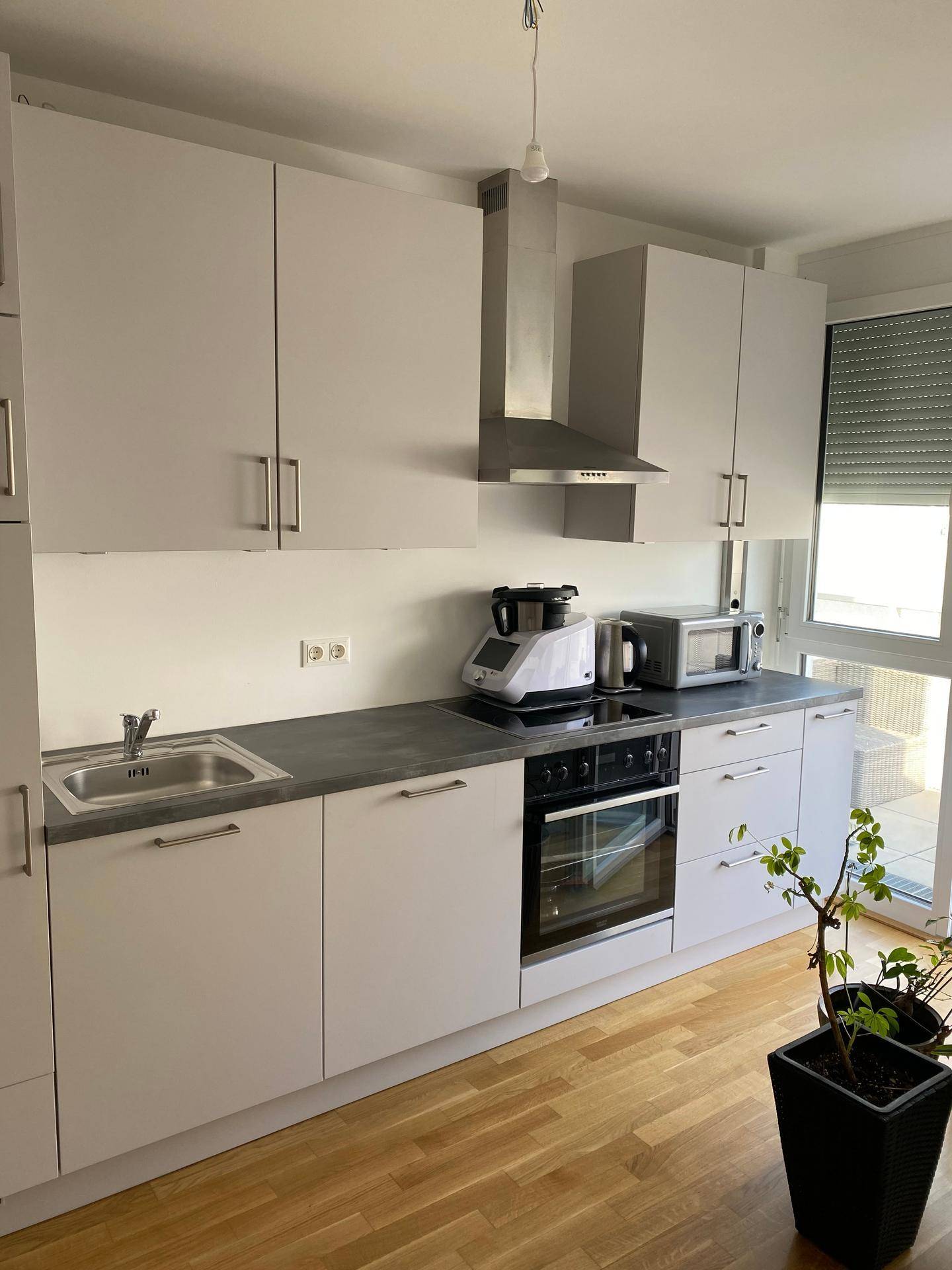 Moderne Einbauküche mit hellgrauen Schränken, dunkler Arbeitsplatte und integrierten Geräten.