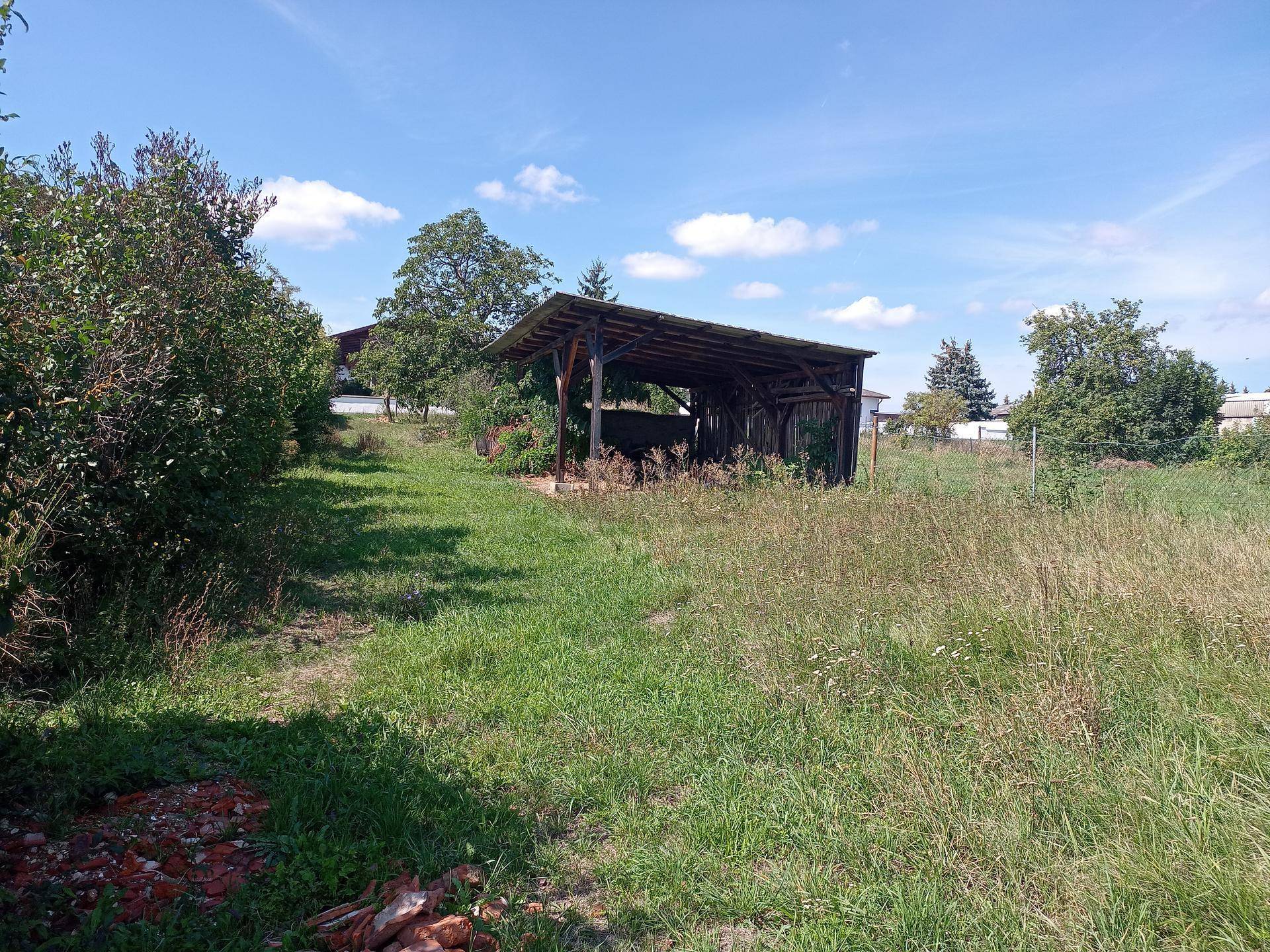 Weitläufiges, grasbewachsenes Grundstück mit einem einfachen Holzunterstand unter klarem Sommerhimmel.