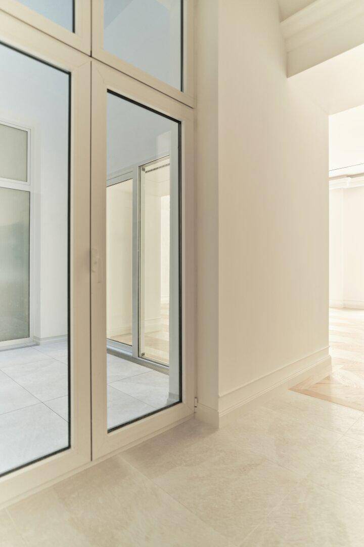 Detailaufnahme einer modernen Glastür mit schlankem Rahmen, die zu einem hellen Bereich führt.