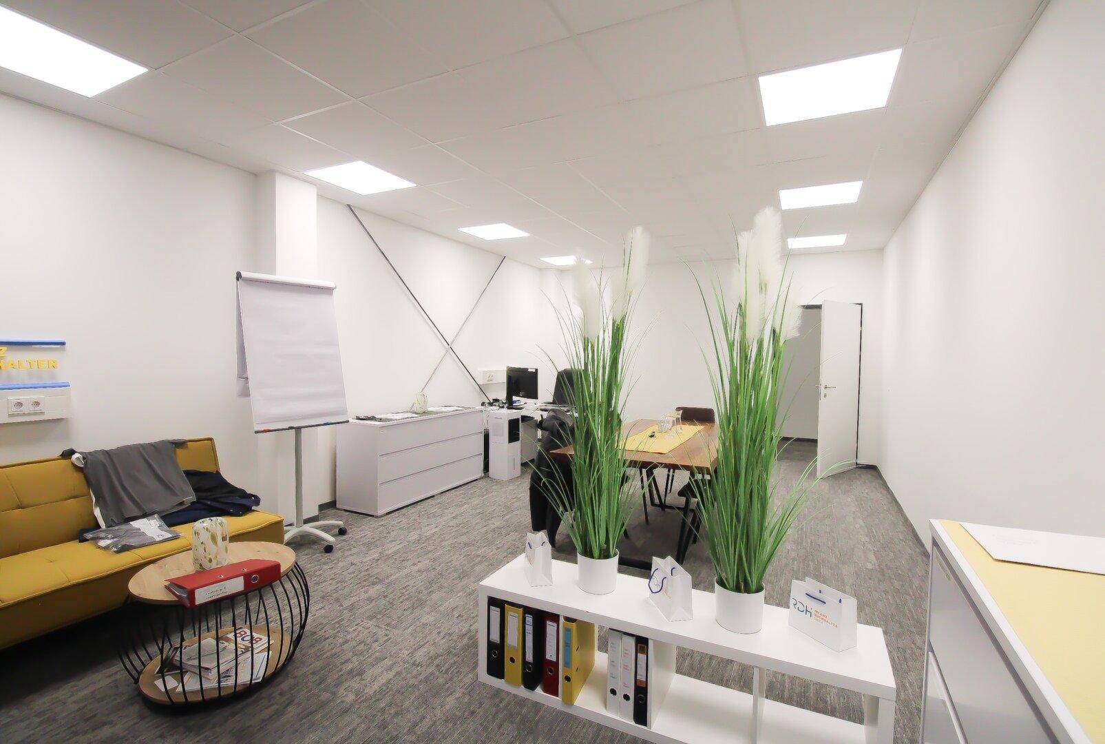 Heller und moderner Büroraum mit gelbem Sofa, Schreibtisch und Besprechungstisch, ausgestattet mit Teppichboden.