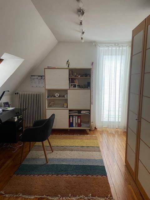 Dachzimmer mit schrägen Decken, Holzboden und einem Arbeitsbereich mit Schreibtisch und Regal.