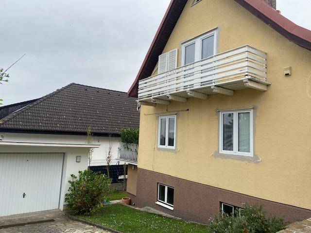 Seitenansicht des gelben Hauses mit Garage und einem leicht abfallenden Rasenbereich.