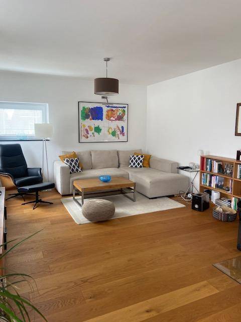 Helles Wohnzimmer mit beigem Ecksofa, Holzboden und modernem Kunstwerk an der Wand.