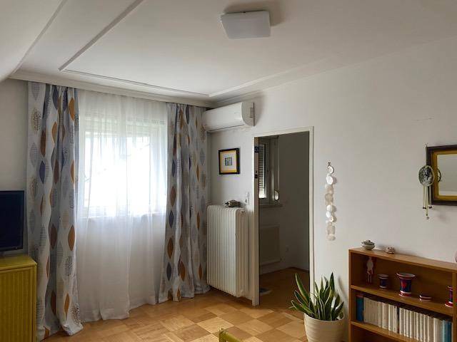Heller Raum mit Parkettboden, Fenster mit Vorhängen und Klimaanlage an der Wand.