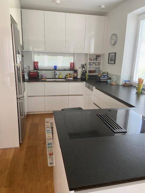 Moderne Küche mit weißen Hochglanzschränken, dunklen Arbeitsplatten und Induktionskochfeld.