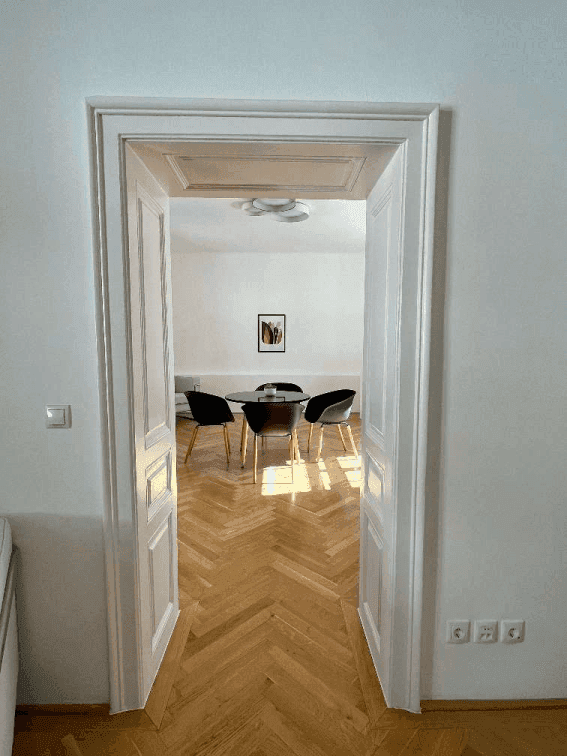 Blick durch eine klassische Tür in einen hellen Wartebereich mit modernem Tisch und Stühlen.