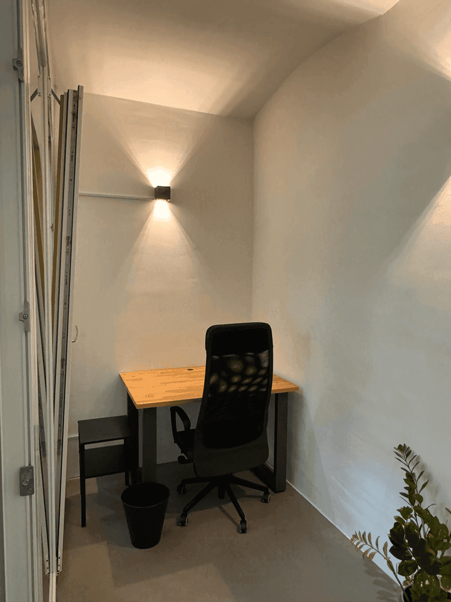 Kleiner, privater Büroraum mit einem Schreibtisch, Bürostuhl und einer Wandleuchte, ideal für konzentriertes Arbeiten.