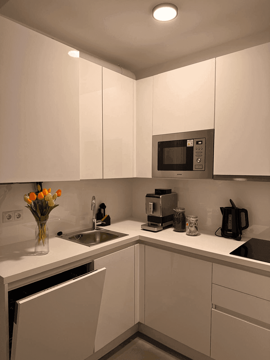 Moderne weiße Küche mit Hochglanzschränken, Einbaumikrowelle, Spülmaschine und Kaffeemaschine.