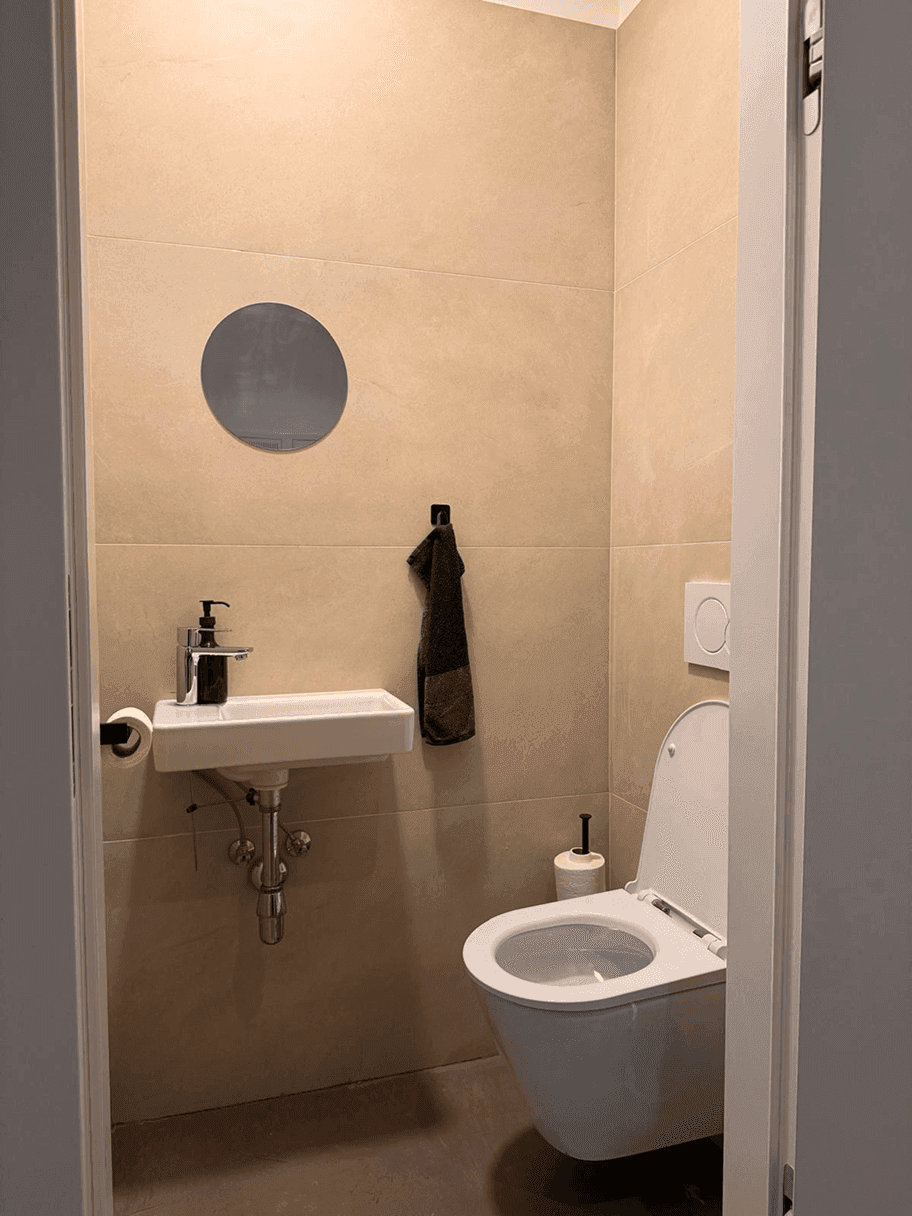 Kleines Gäste-WC mit wandhängender Toilette, einem Waschbecken und beigefarbenen Fliesen.