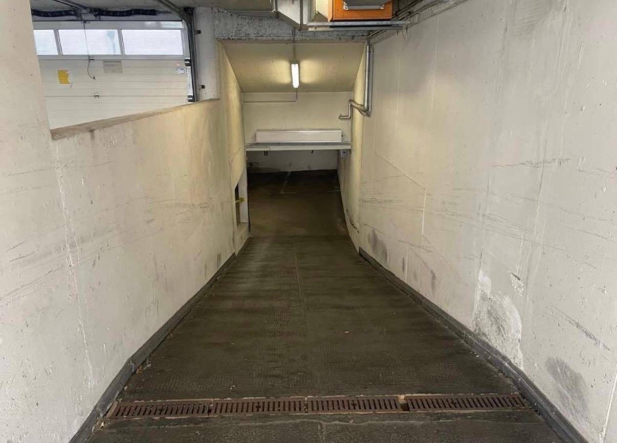 Betonrampe führt hinab in eine Tiefgarage mit Entwässerungsrinne am Eingang.