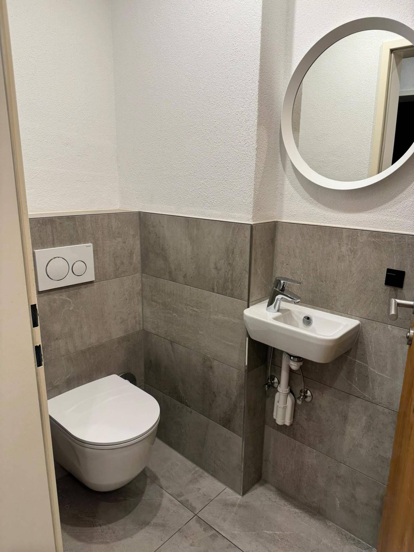 Modernes Gäste-WC mit Wand-WC, kleinem Waschbecken und stilvollen grauen Fliesen an Wänden und Boden.
