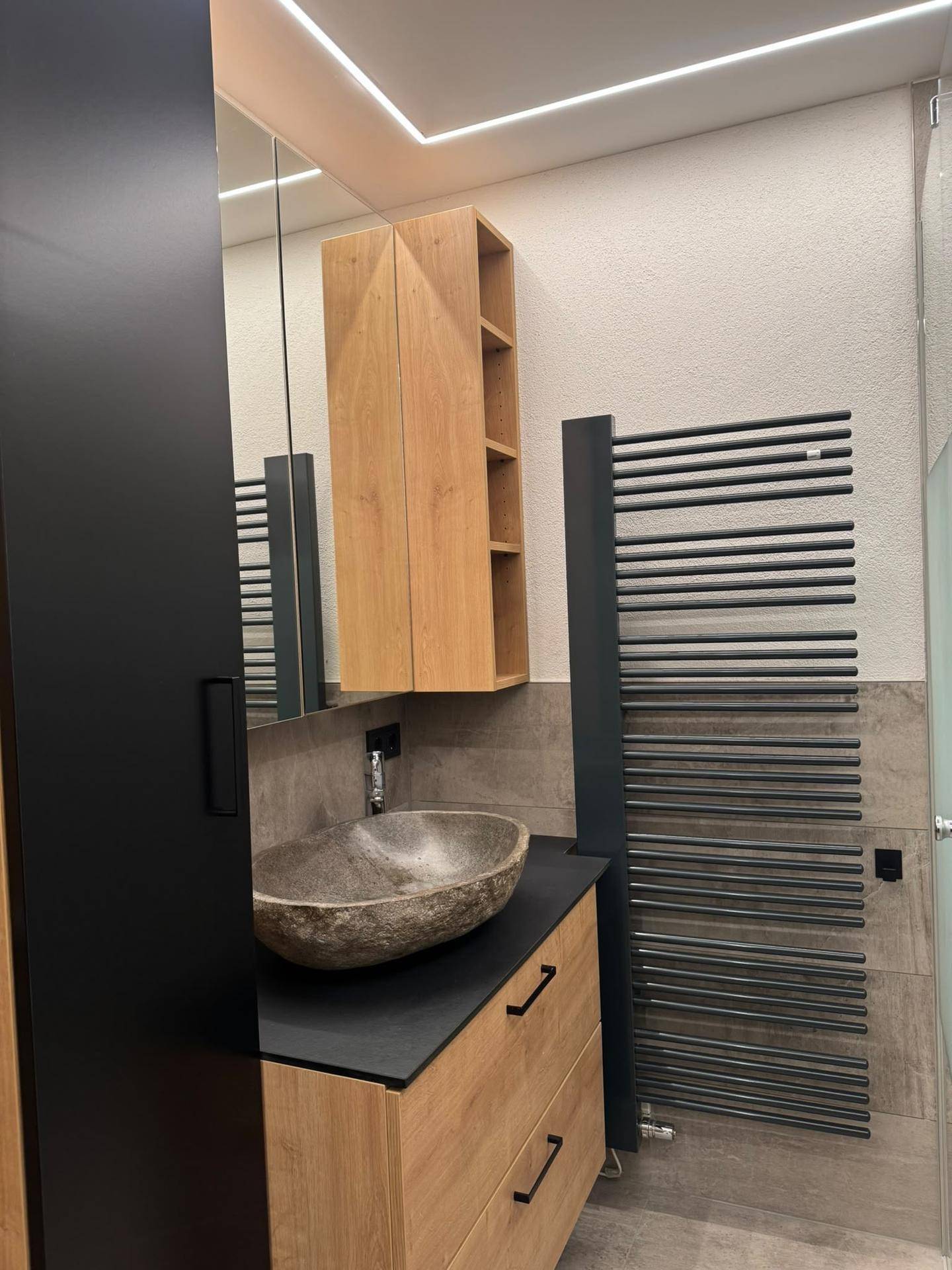 Modernes Badezimmer mit Natursteinwaschbecken, Holzunterschrank, Spiegelschrank und beheiztem Handtuchhalter.