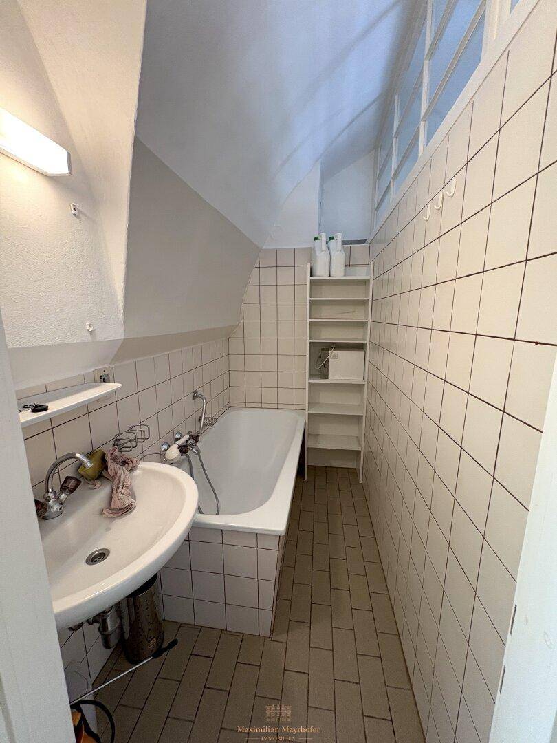Kleines Badezimmer mit Badewanne, Waschbecken und weißen Fliesen unter einer Dachschräge.