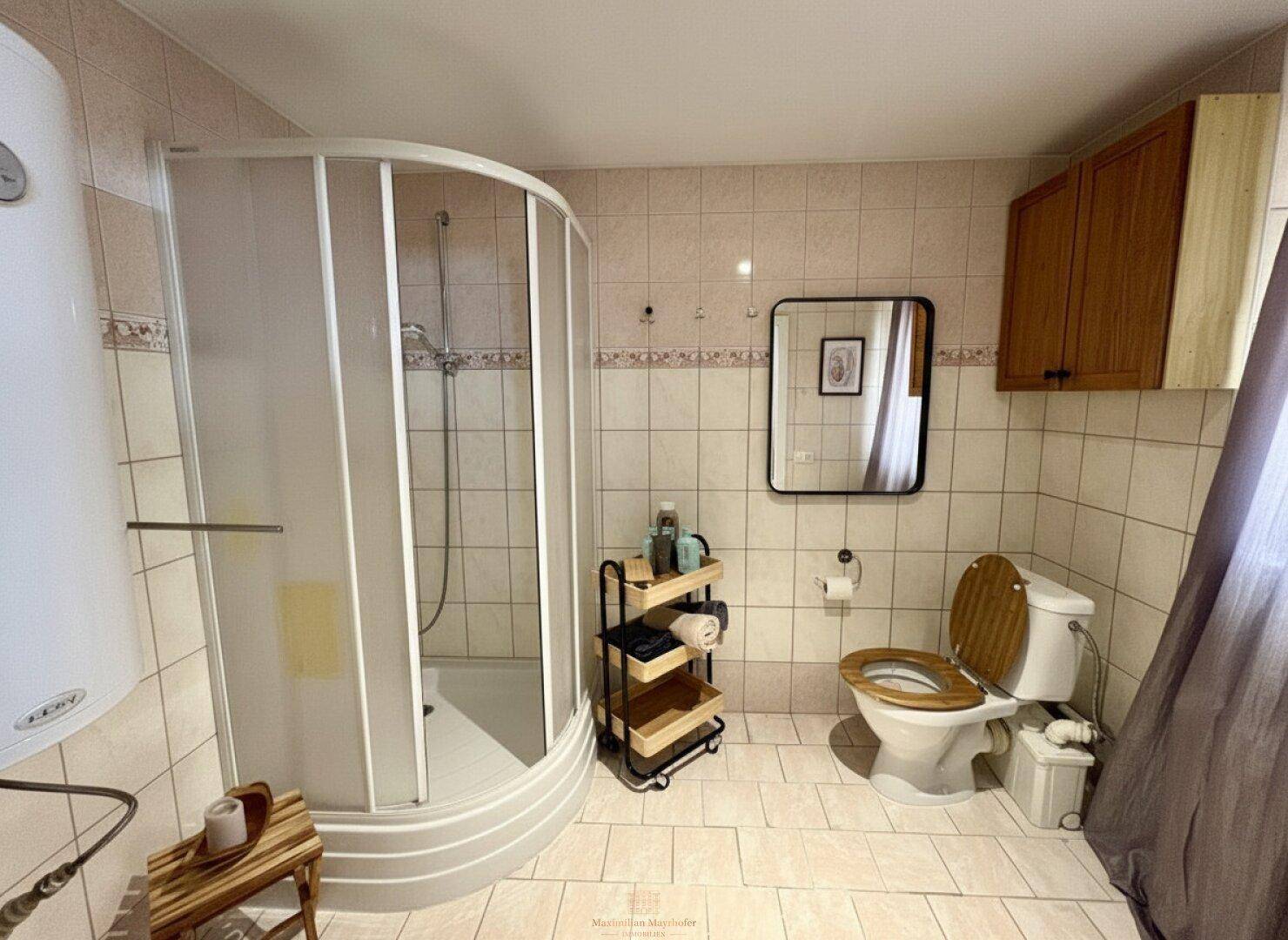 Gefliestes Badezimmer mit Duschkabine, Toilette und einem kleinen Holzregal.