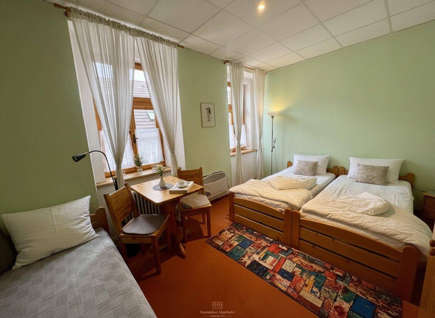 Helles Schlafzimmer mit zwei Einzelbetten, einem Beistelltisch und grünen Wänden.