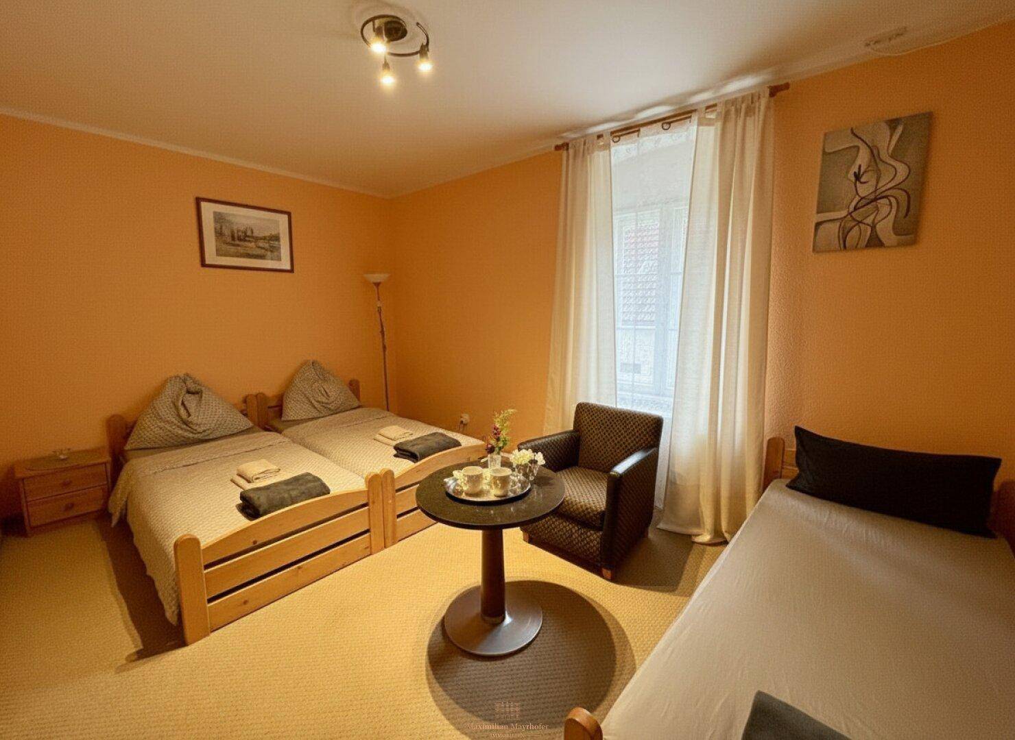 Gemütliches Schlafzimmer mit zwei Einzelbetten, einem Sessel und orangefarbenen Wänden.