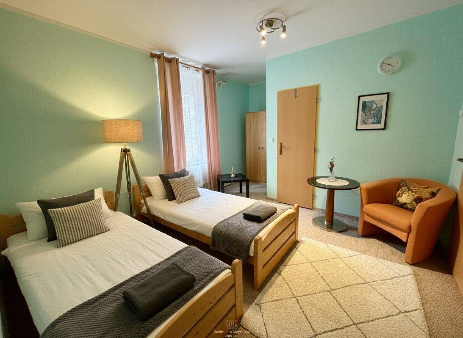 Helles Schlafzimmer mit zwei Einzelbetten, einem Sessel und mintgrünen Wänden.